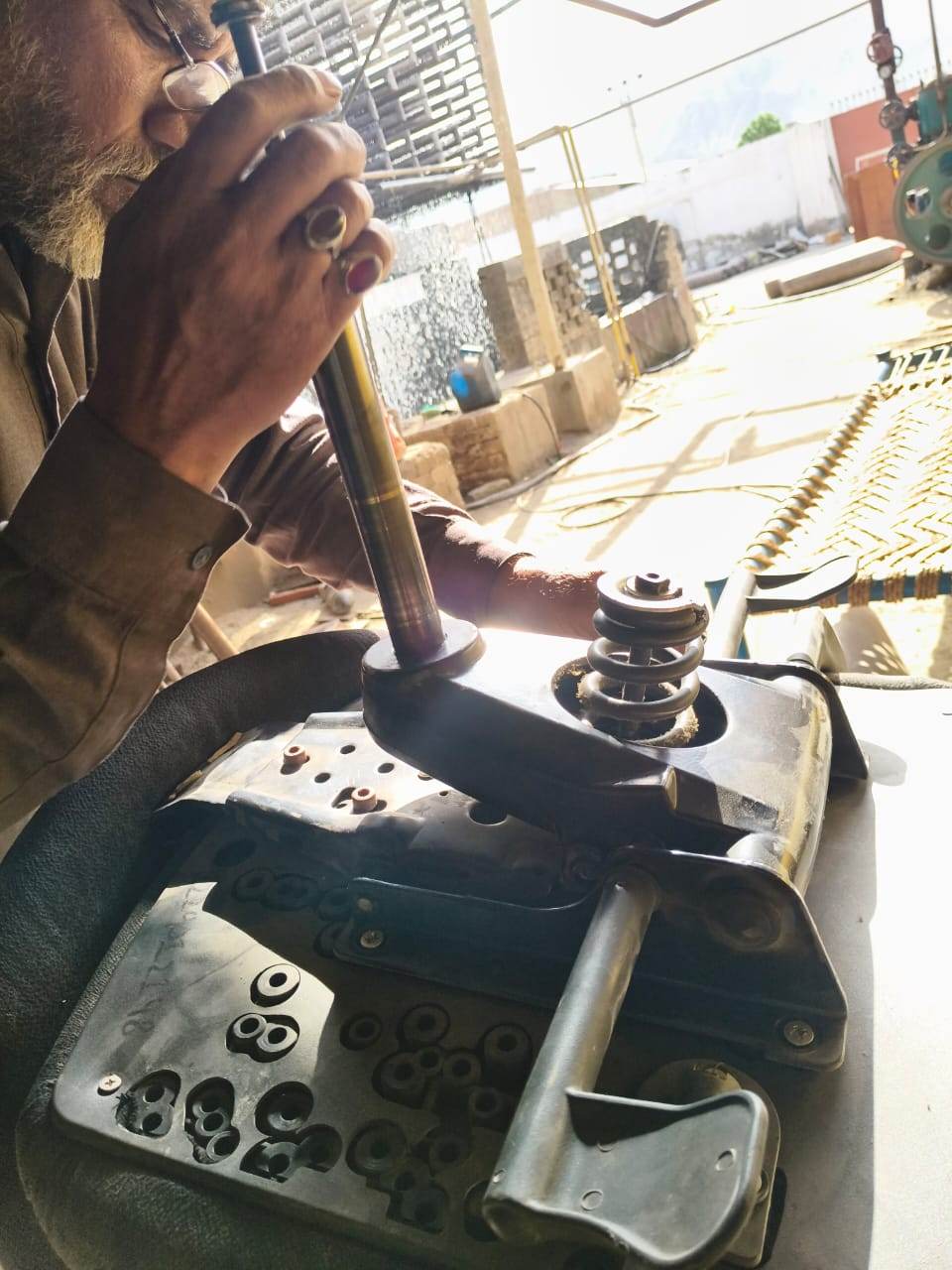 The upholsterer fitting a gas lift cylinder into the tilt mechanism of a stripped office chair on his workbench.